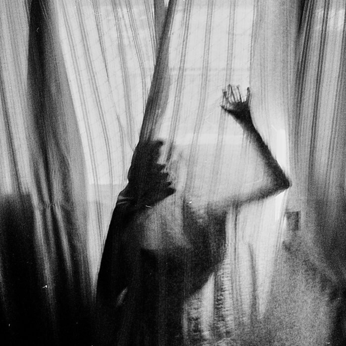 Silhouette of a person behind sheer curtains creates an eerie mood.